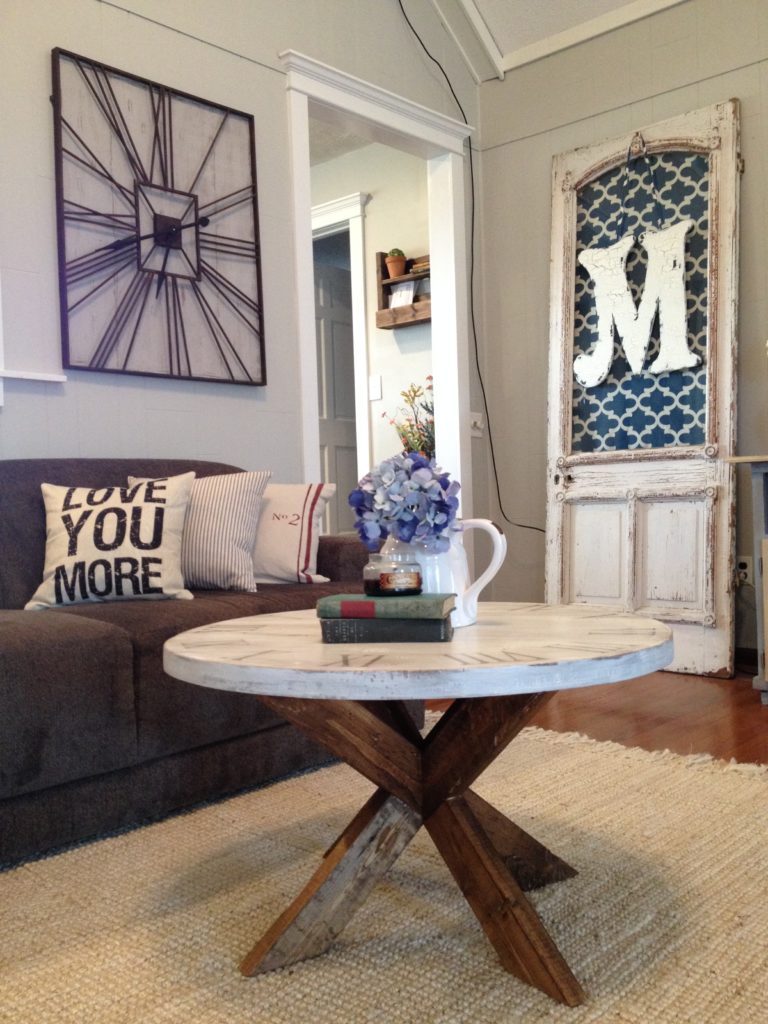 Round coffee table with wood X base and white round top on rug in living room in front of couch