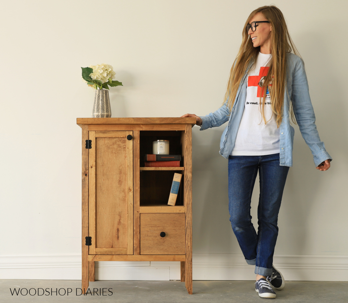 Shara Woodshop Diaries standing next to DIY accent cabinet with door on left side and open shelves with drawer on the right side 