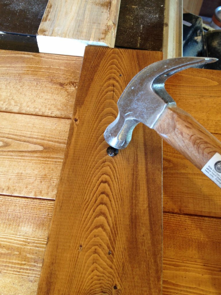 Hammer nailing decorative nail heads onto wood boards