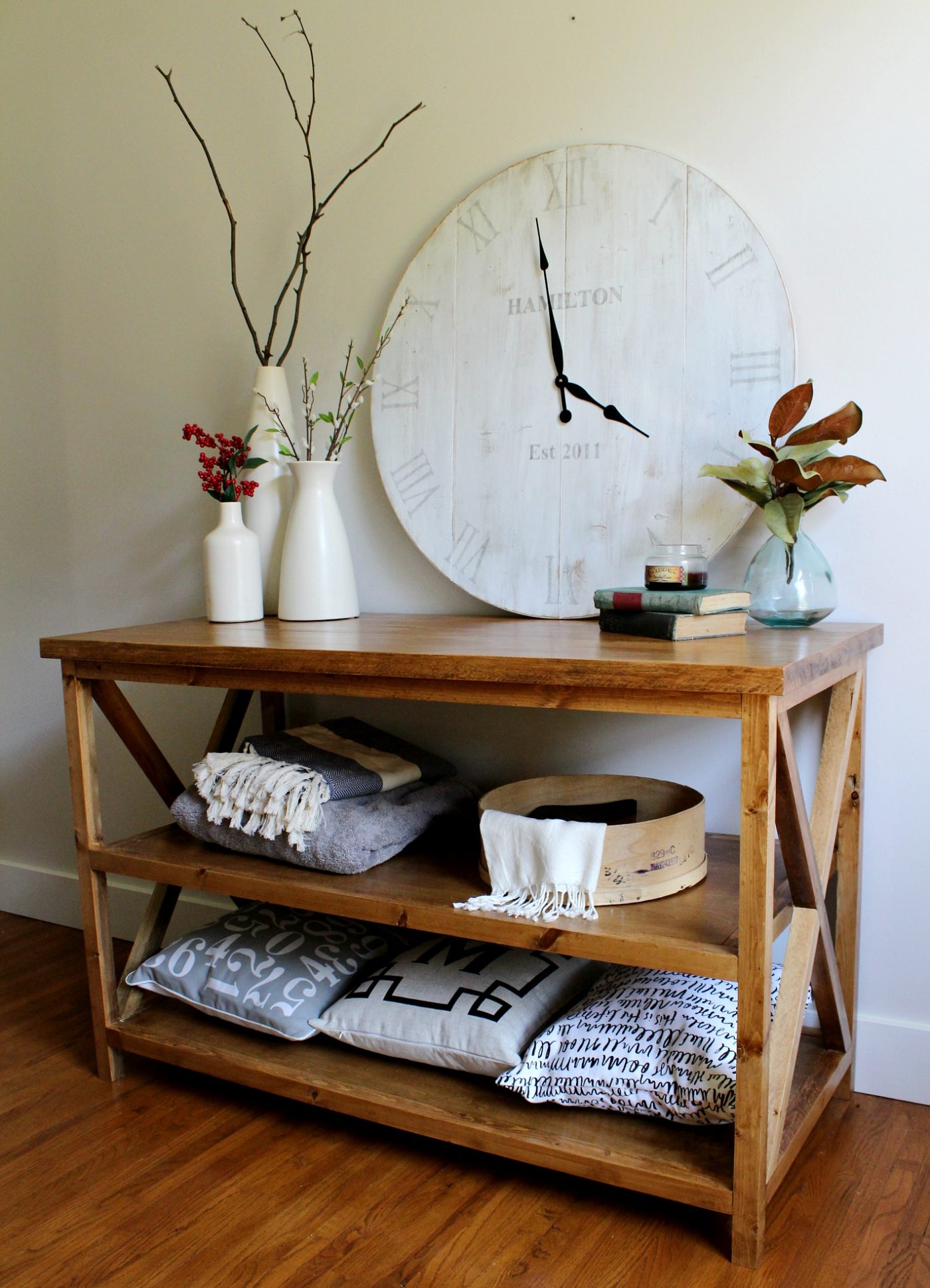 DIY X base console table with middle shelf finished and filled with pillows and blankets with decor on top