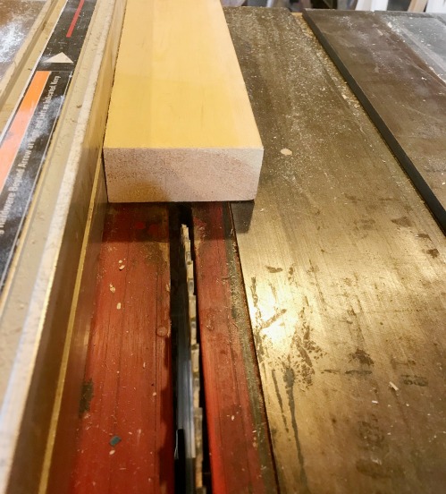 2x4 board on table saw with square edge against rip fence set to cut 1 ½"