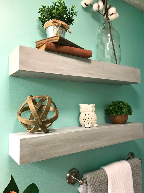 DIY floating wall shelves on a light green wall over a towel bar.