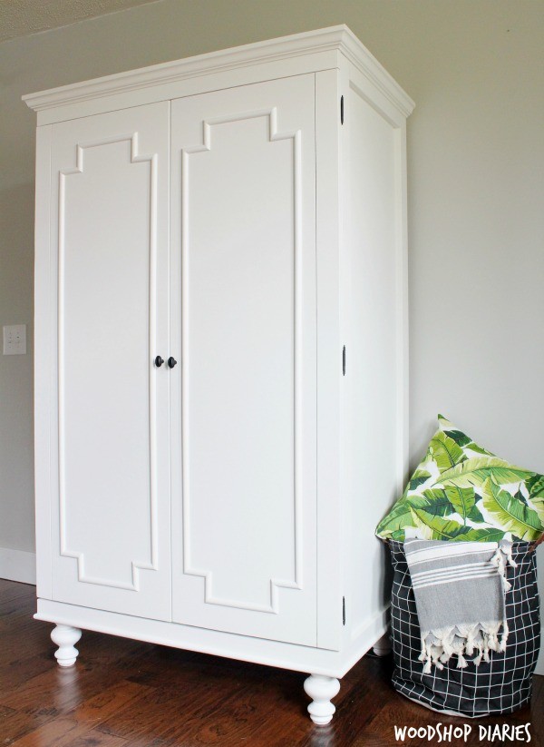 White armoire with double doors trimmed out with half round molding and black hardware accents