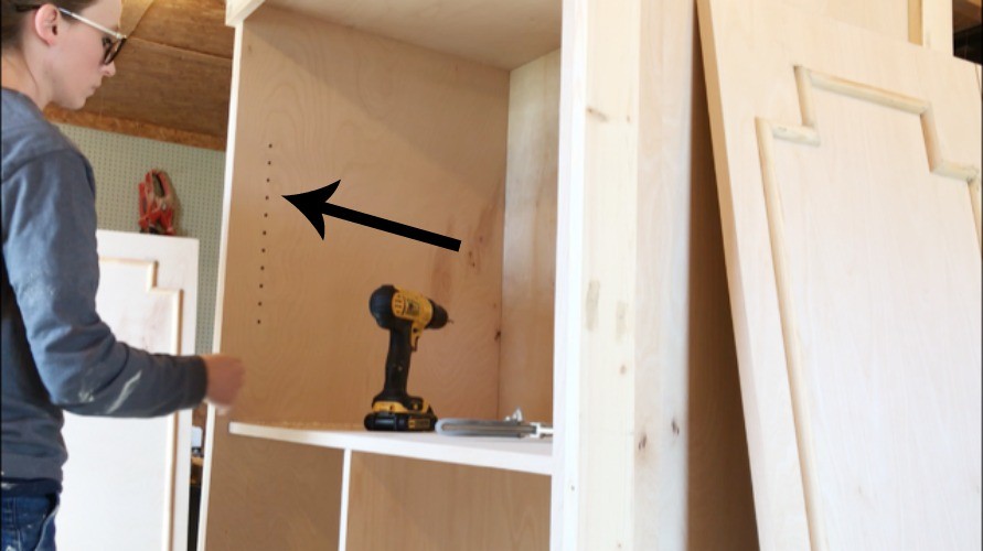 Inside of plywood cabinet with arrow pointing to shelf pin holes