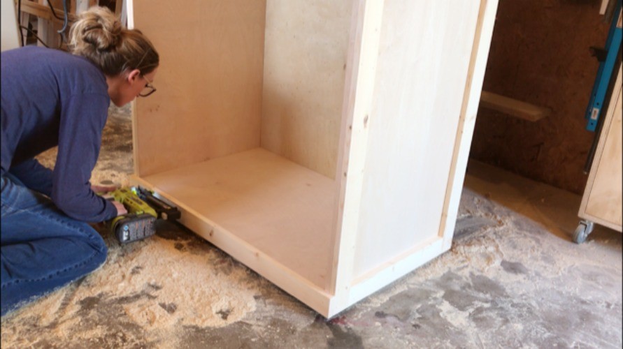 Shara Woodshop Diaries brad nailing 1x3 trim pieces along bottom edge of cabinet