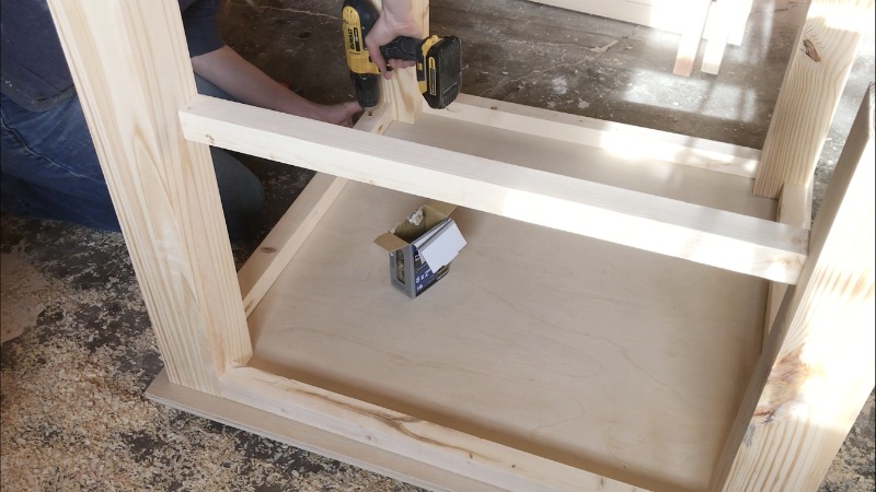 Using a drill to attach kids table top to table base upside down on workshop floor