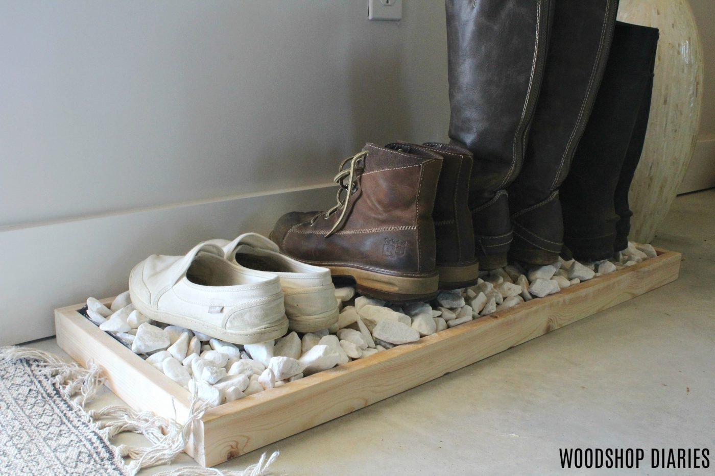 Wooden boot tray with white decorative rocks with boots and shoes on top