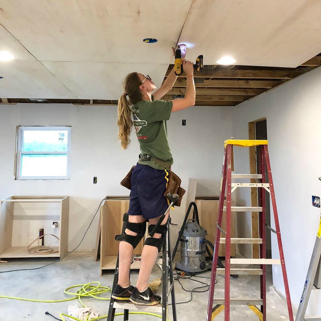 Shara screwing plywood panels into trusses on ceiling of garage apartment