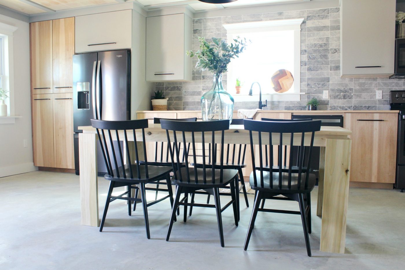 Contemporary modern dining table in kitchen with black chairs and grey backsplash