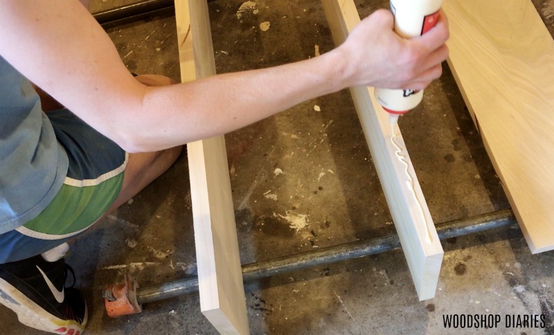 apply glue to headboard panel on DIY modern bed frame