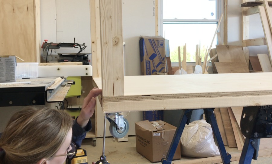 Shara Woodshop Diaries installing caster wheels on bottom of mobile workbench