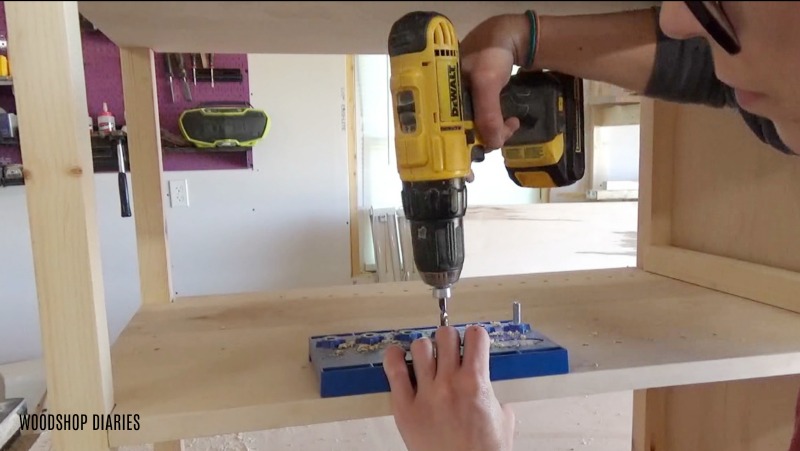 Using drill and Kreg shelf pin jig to drill out adjustable shelf pin holes in laundry cabinet