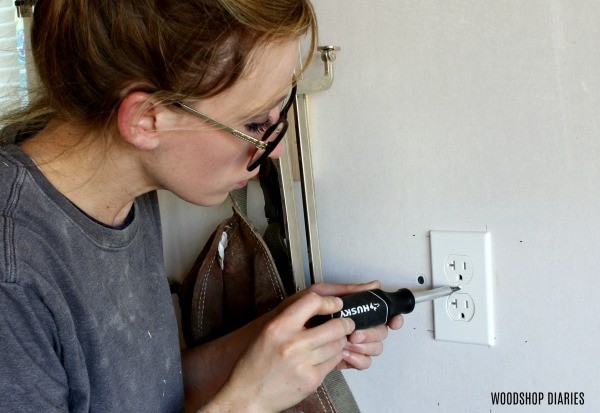 Using screwdriver to tighten outlet covers in workshop