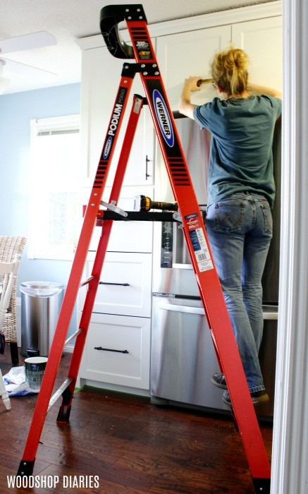 Using ladder to install cabinet hardware in kitchen cabinet doors--gift idea number 10 for new homeowners