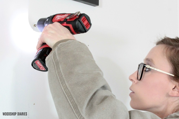 Using battery powered drill to drive screw to hang picture