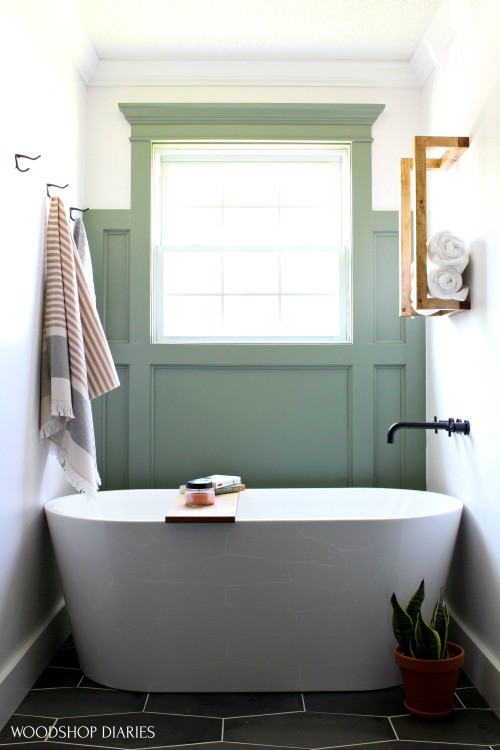 Freestanding tub in bathroom nook with scrap wood towel rack hanging above it with towels stacked