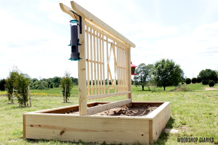 DIY Garden bed with trellis design sitting in yard with birdfeeders hanging on sides
