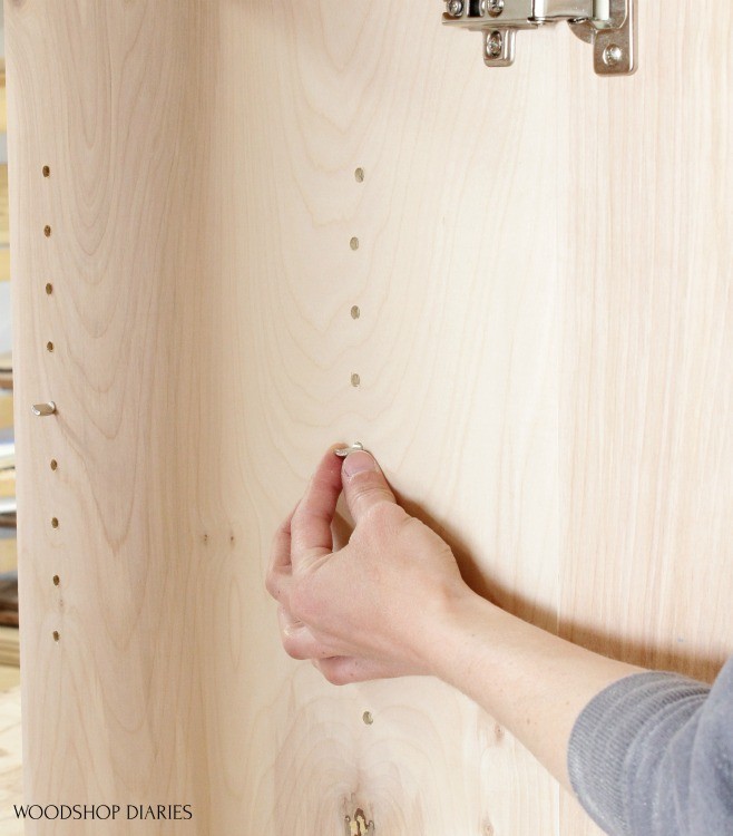 Placing shelf pin in shelf pin holes in plywood cabinet for adjustable shelves