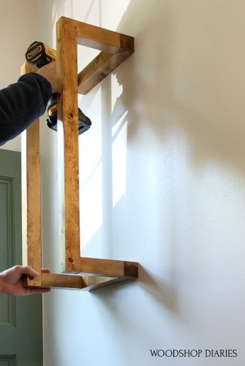 Shara attaching towel rack to wall using driver and 3" wood screws