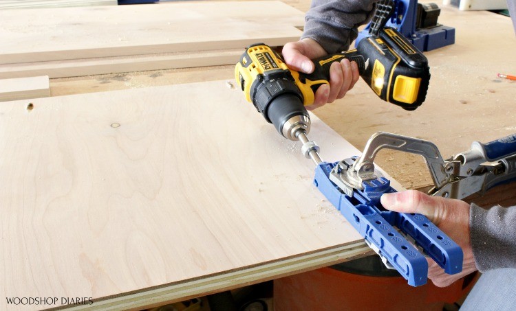 Kreg 320 jig clamped to plywood panel with drill drilling pocket hole