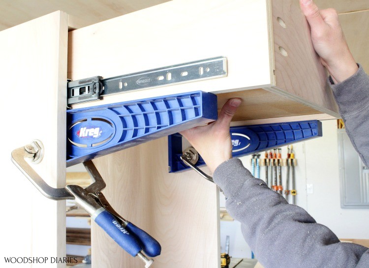 Installing drawer box into cabinet on top of drawer slide jigs clamped to cabinet carcass