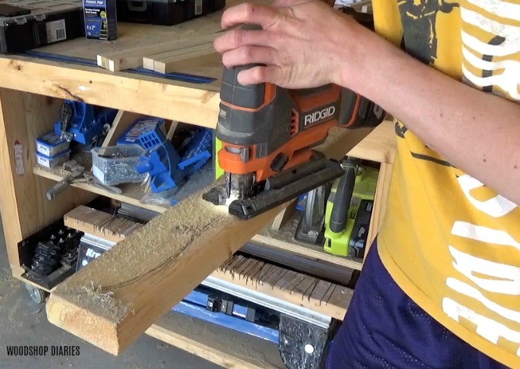 Using a jig saw to cut pergola design shape into top boards of decorative garden bed trellis