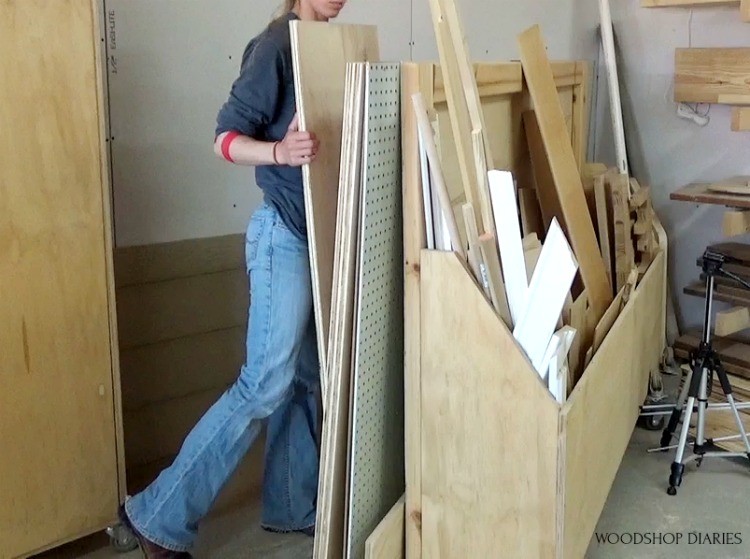Shara picking up a piece of plywood from behind her scrap wood bin
