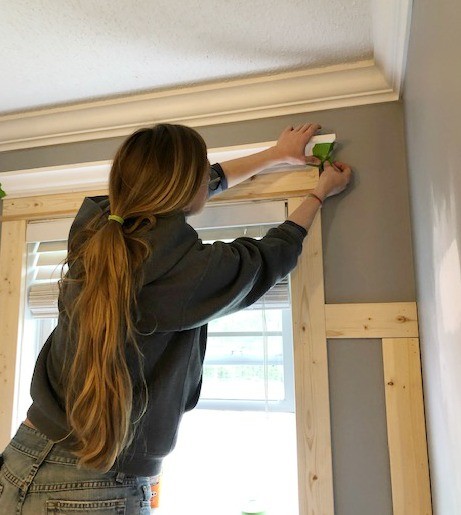 Shara taping crown molding around window trim on master bathroom feature wall