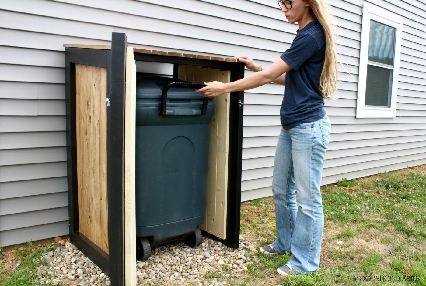 Shara Woodshop Diaries pulling trash can out of trash can cover with door open