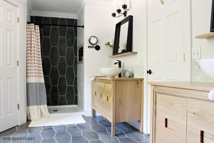 Wide view of master bathroom white oak double vanities, black mirrors, and two tone shower nook