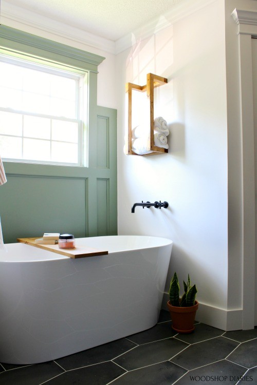 Free standing bathtub in bathroom nook with green feature wall and towel rack