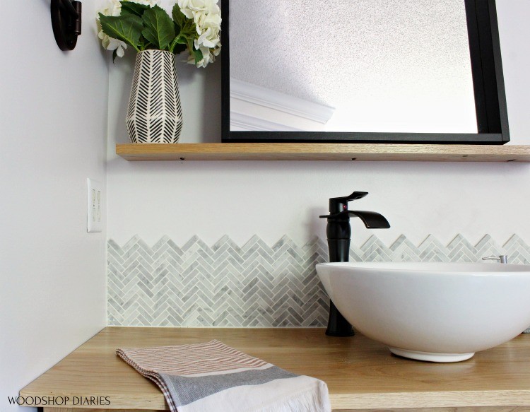 Close up of Jet Stream backsplash tile over top of white oak vanity with black framed mirror on floating shelf