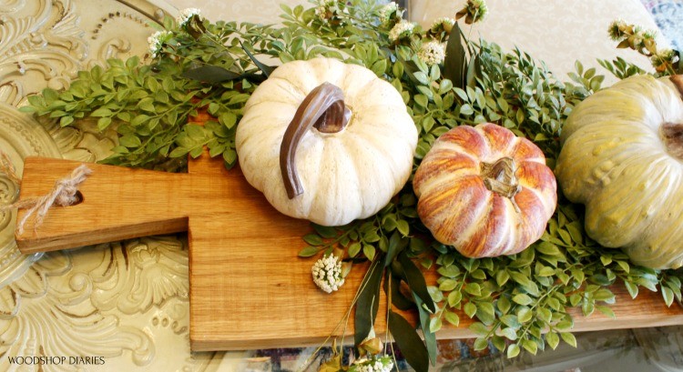 top end of serving board decorated with pumpkins and greenery