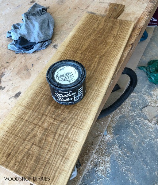 Can of furniture butter sitting on finished serving board with rough saw marks