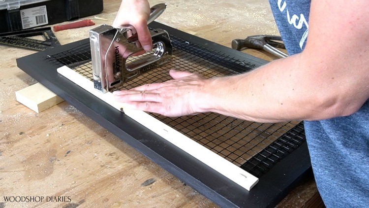 Stapling scrap wood blocks on back side of door to cover mesh edges