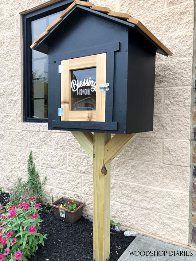 Top to Bottom view of black and cedar blessing birdhouse donation box in front of studio building