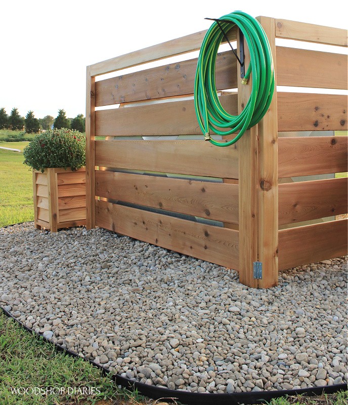 Louvered planter box at corner of faux fence well house cover with red mum sitting in it