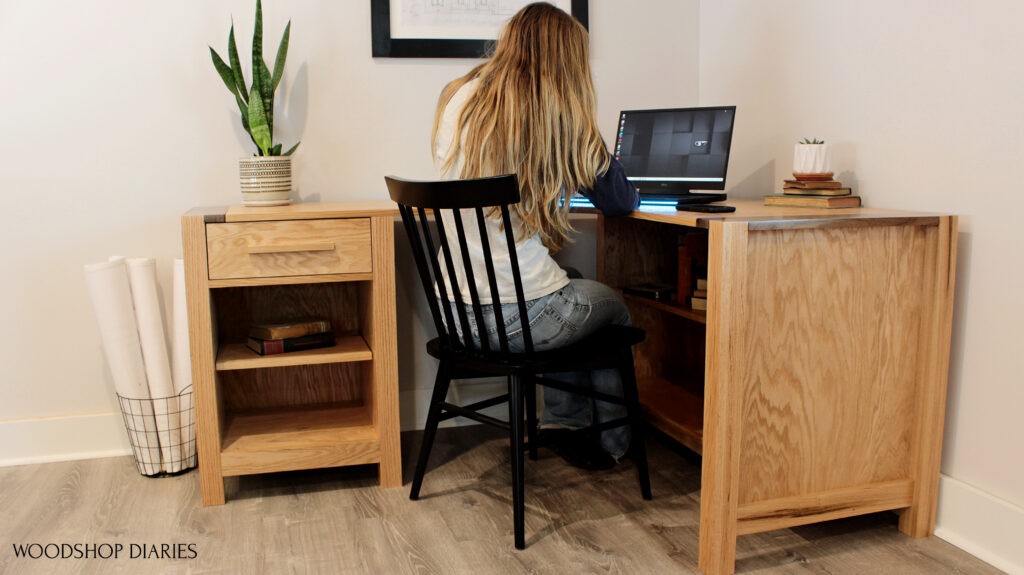 Shara Woodshop Diaries sitting at DIY L shaped desk corner desk with shelves