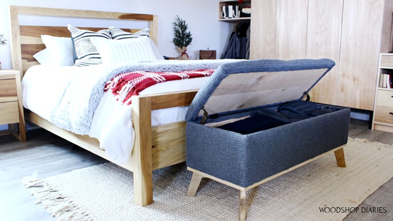 Storage bench with lid open full of blankets and clothes at end of bed