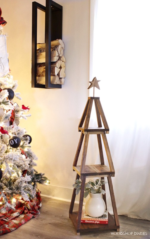 Stackable Christmas tree shelf set up next to Christmas tree with decor sitting on it