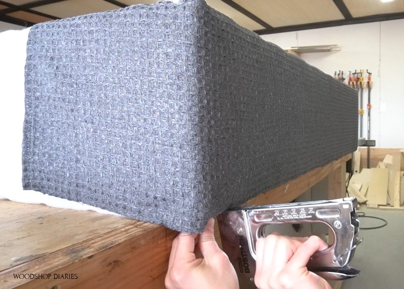 Using staple gun to secure fabric on underside of bench storage box