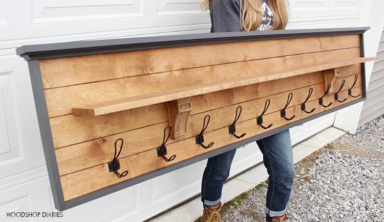 Angled view of Shara holding DIY coat rack with shelf in front of garage door