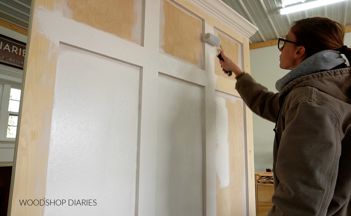 Shara Woodshop Diaries applying primer to DIY furniture piece in workshop with roller 