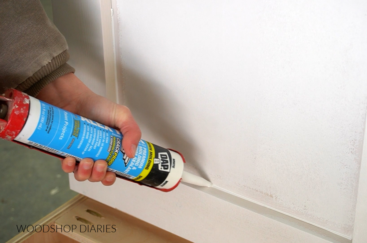 Close up of applying trim caulk to inside corners of DIY furniture project after primer and before paint