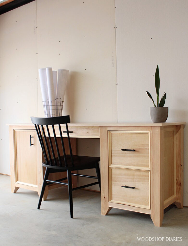 Finished DIY computer desk with two drawers on right, keyboard tray in center, and door on left side with black chair--made from 2x4s and plywood