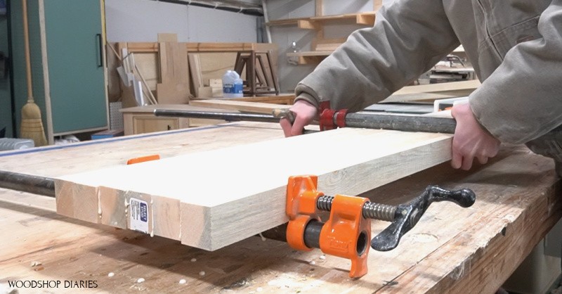 Shara using pipe clamps to glue six 2x2s together to make the first half of the shelf panel