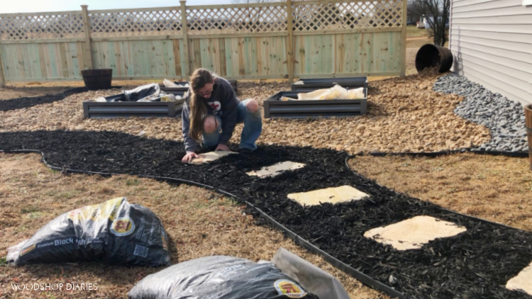 Installing stepping stones in black mulch walkway of backyard makeover