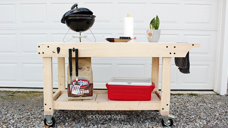 BBQ prep table on wheels with grill on top and cooler below and bag of charcoal ready to cook