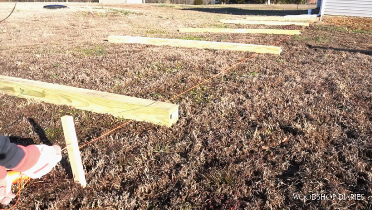 Fence posts laid out on ground with string pulled to keep straight