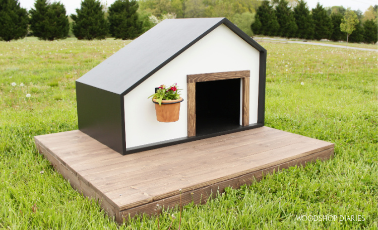 Black and White modern style dog house on wood deck in yard with flower hanging on front